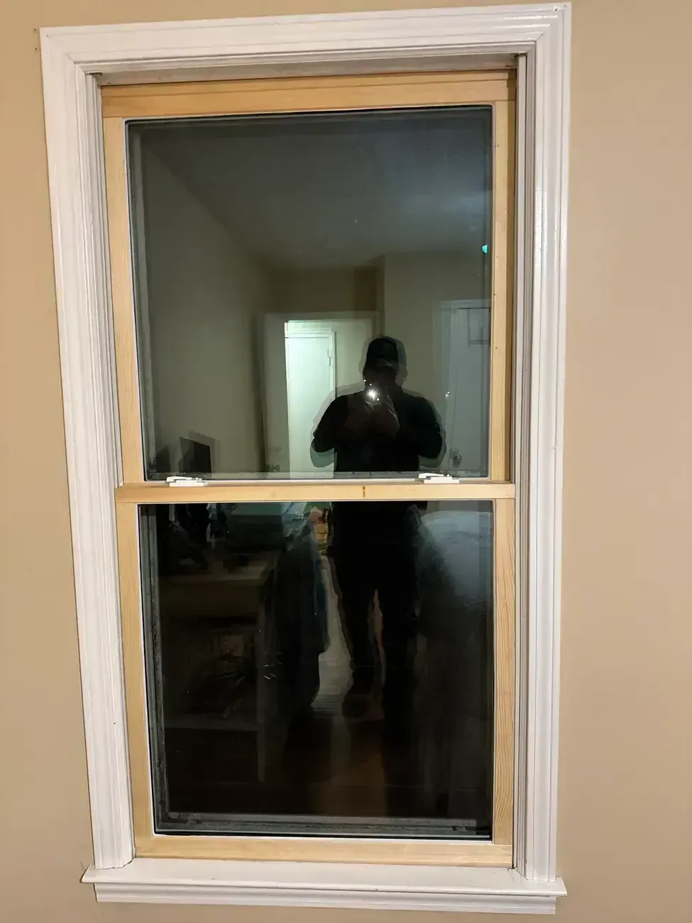 White-framed window with closed blinds and a reflection of a person holding a camera in a room