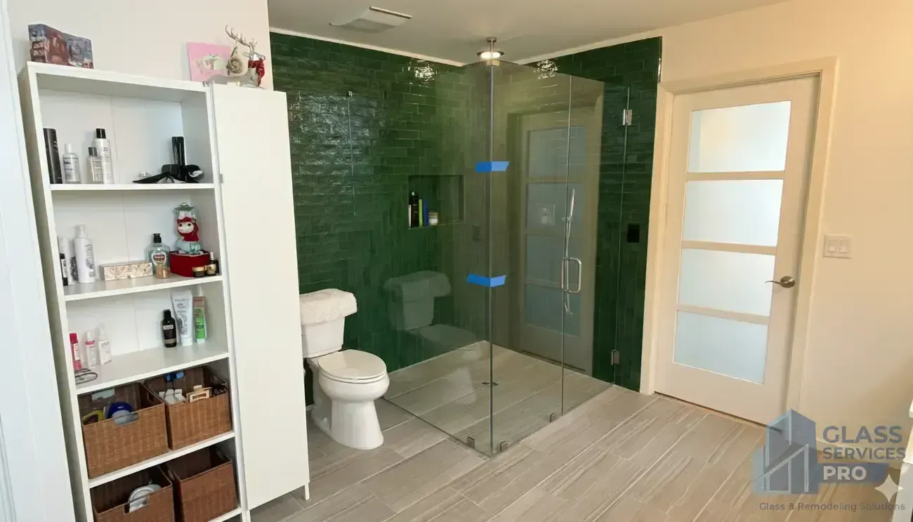 Modern bathroom with glass shower enclosure, white toilet, and built-in shelves; green tile accent wall