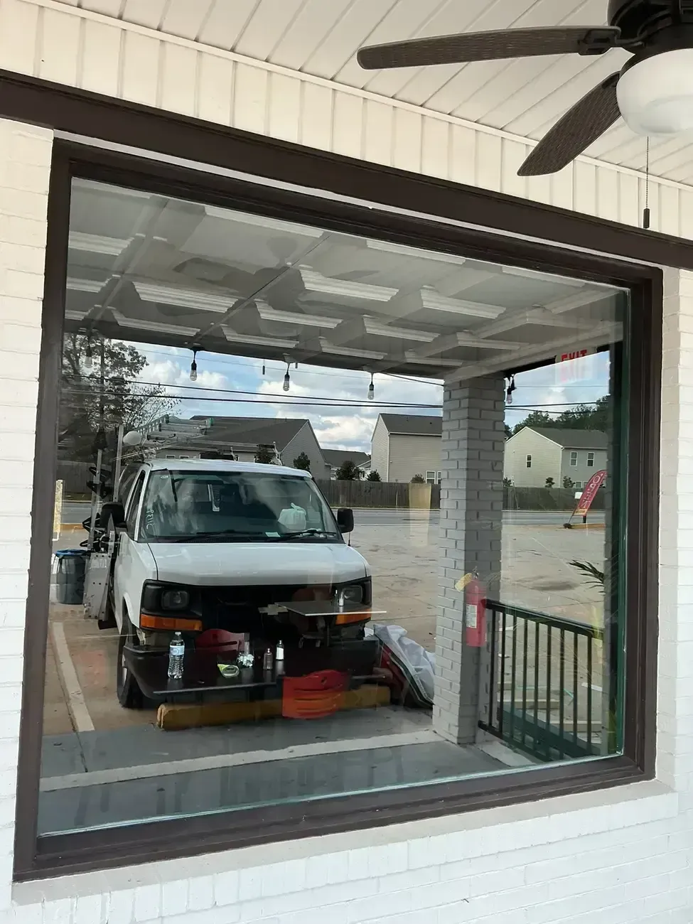 White van parked in a carport, seen through a large window with a ceiling fan overhead.