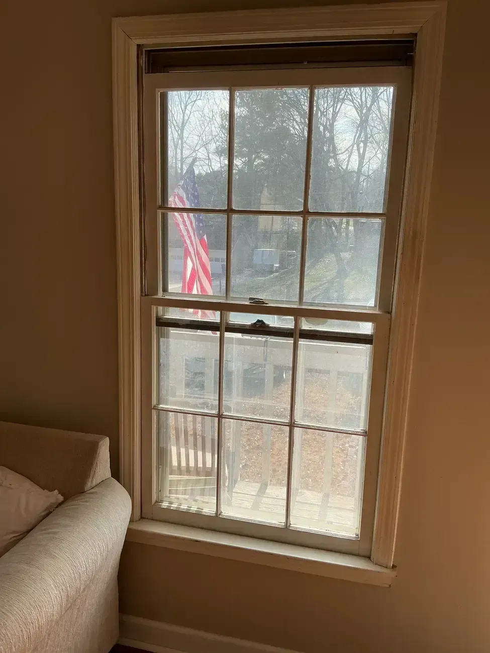 Living room window with a view of an American flag outside and a sofa at left