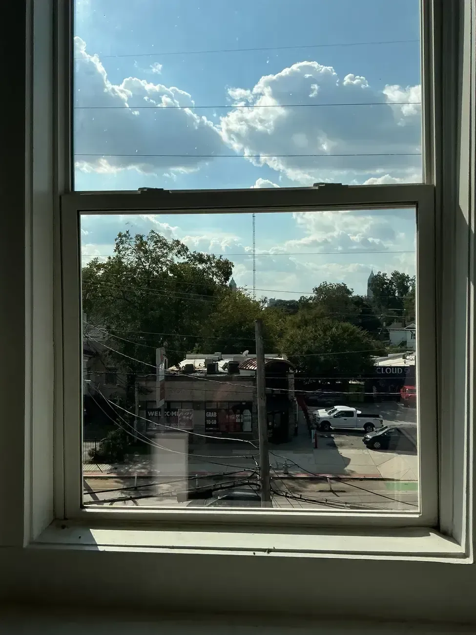 View through a window of a sunny sky with clouds, trees, and a parking lot outside