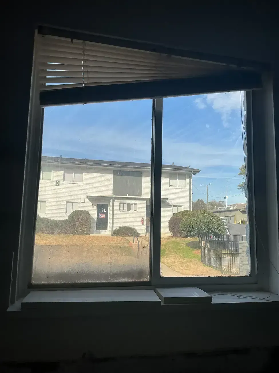 View through a window of a white two-story house, lawn, and blue sky.