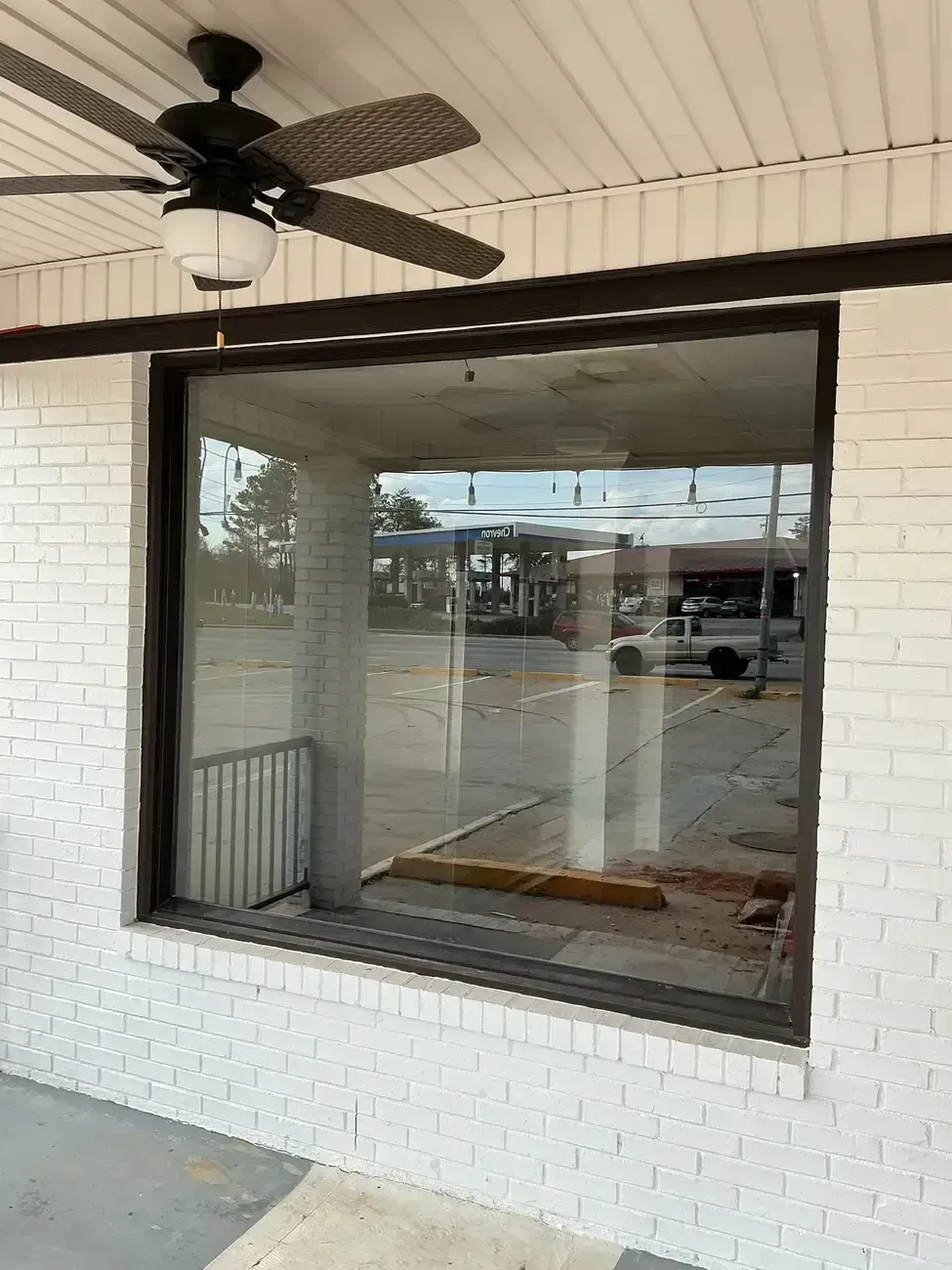 Storefront window with black trim, white brick wall, and a ceiling fan on a covered porch.