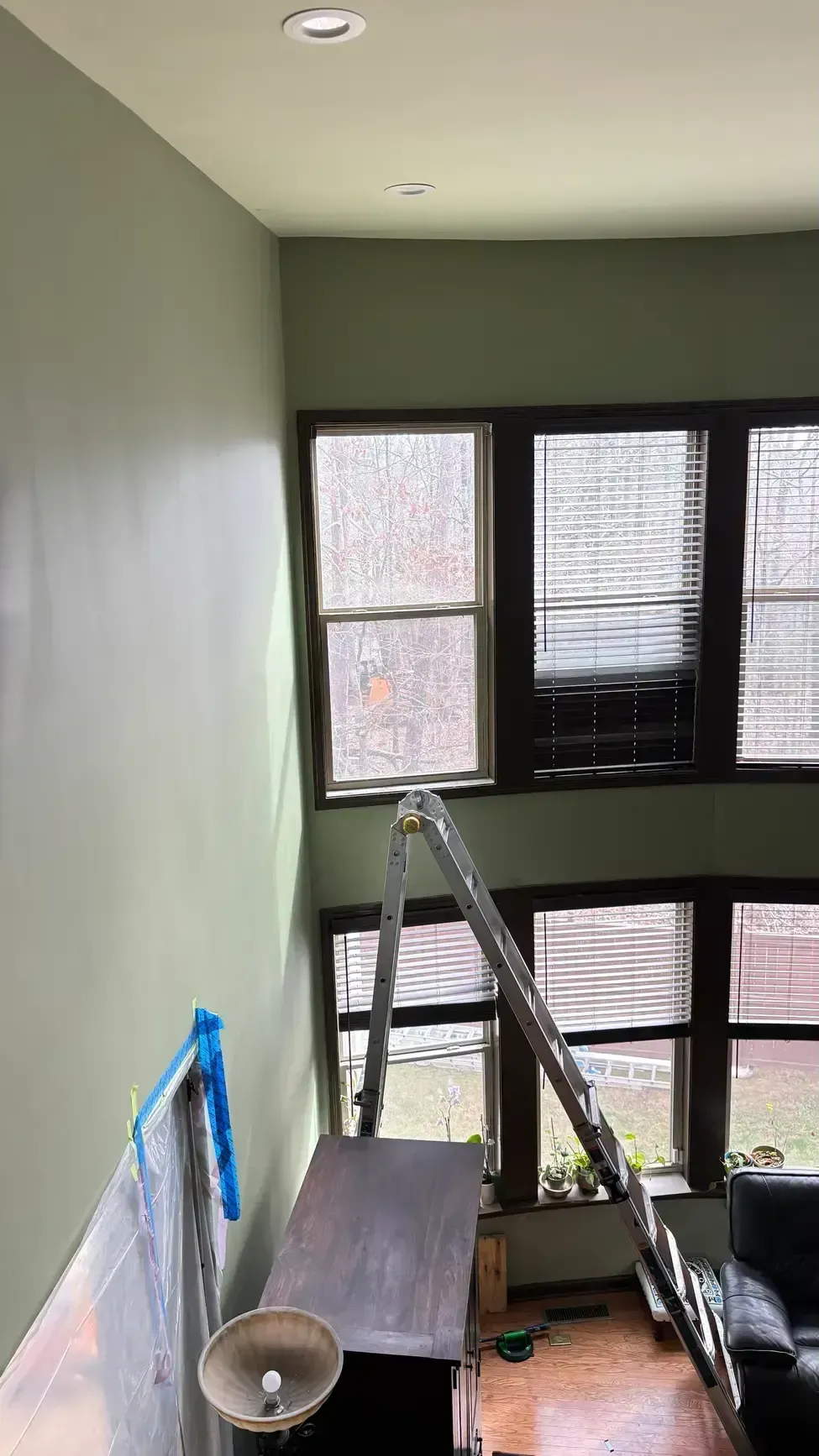 Interior stairwell with green walls, black-framed windows, and a ladder on the landing.