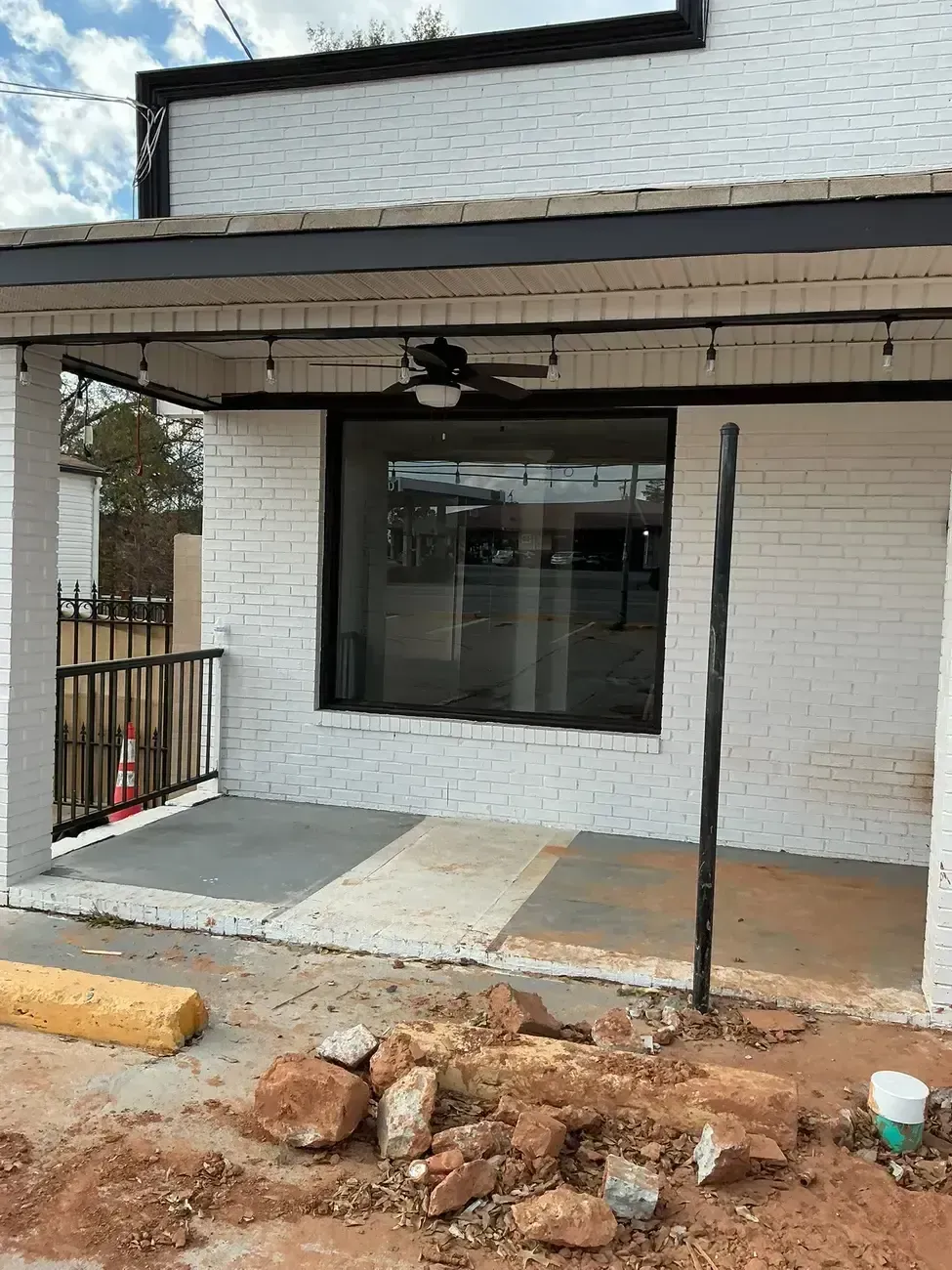 Front porch of a white brick house with a dark awning, large window, and unfinished ground work in front