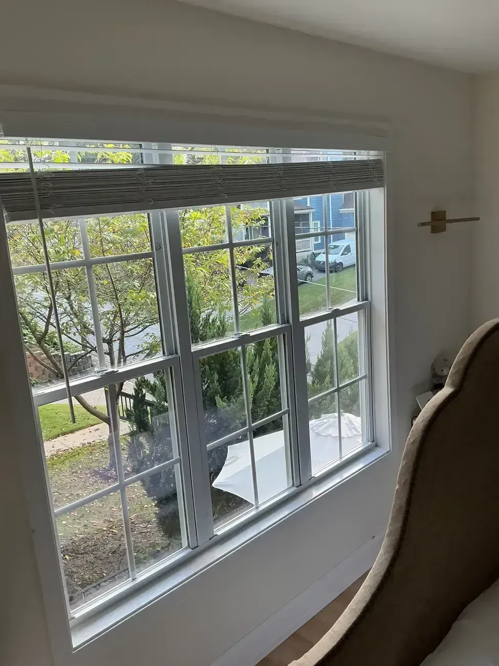 Bedroom window with white blinds, looking out onto trees and parked cars