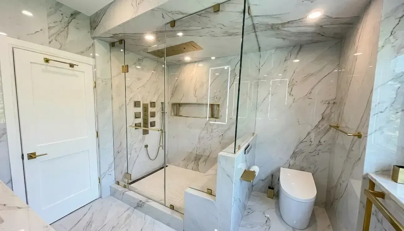 Modern marble-tiled bathroom with glass shower, wall niche, toilet, and gold fixtures