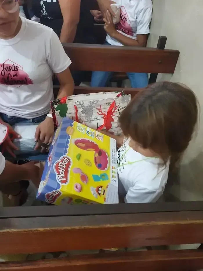 Children gathered around a yellow board game box on a bench indoors, with gift bags nearby