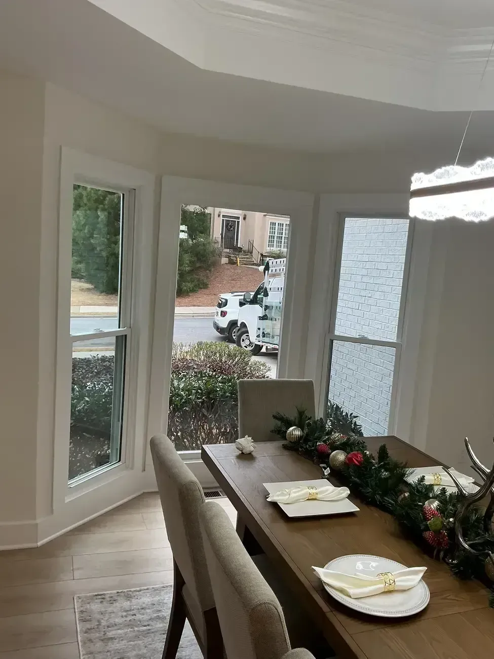 Bright dining room with holiday table setting and garland, viewed through bay windows onto a street outside