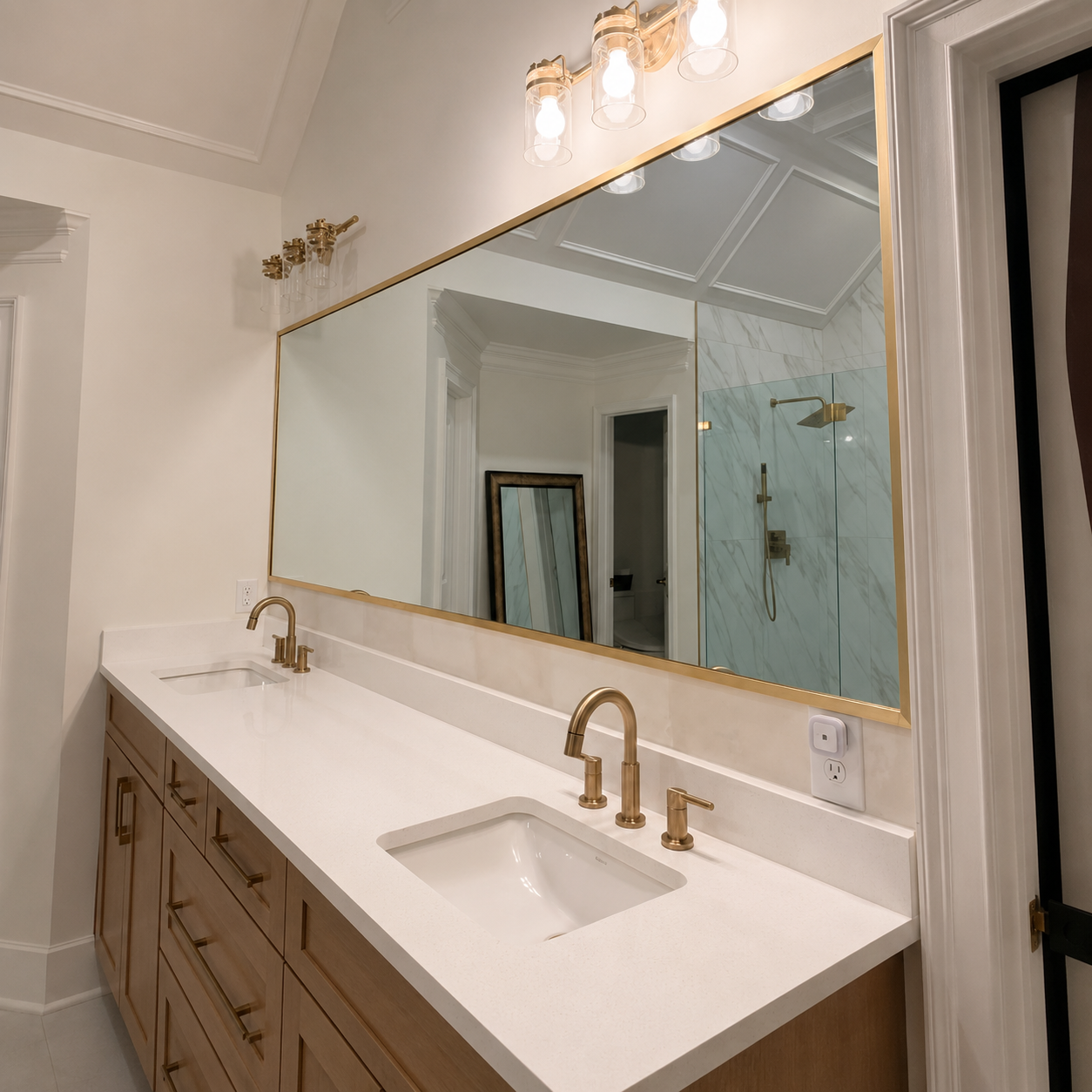 Modern bathroom vanity with double sinks, brass faucets, and a large frameless mirror.