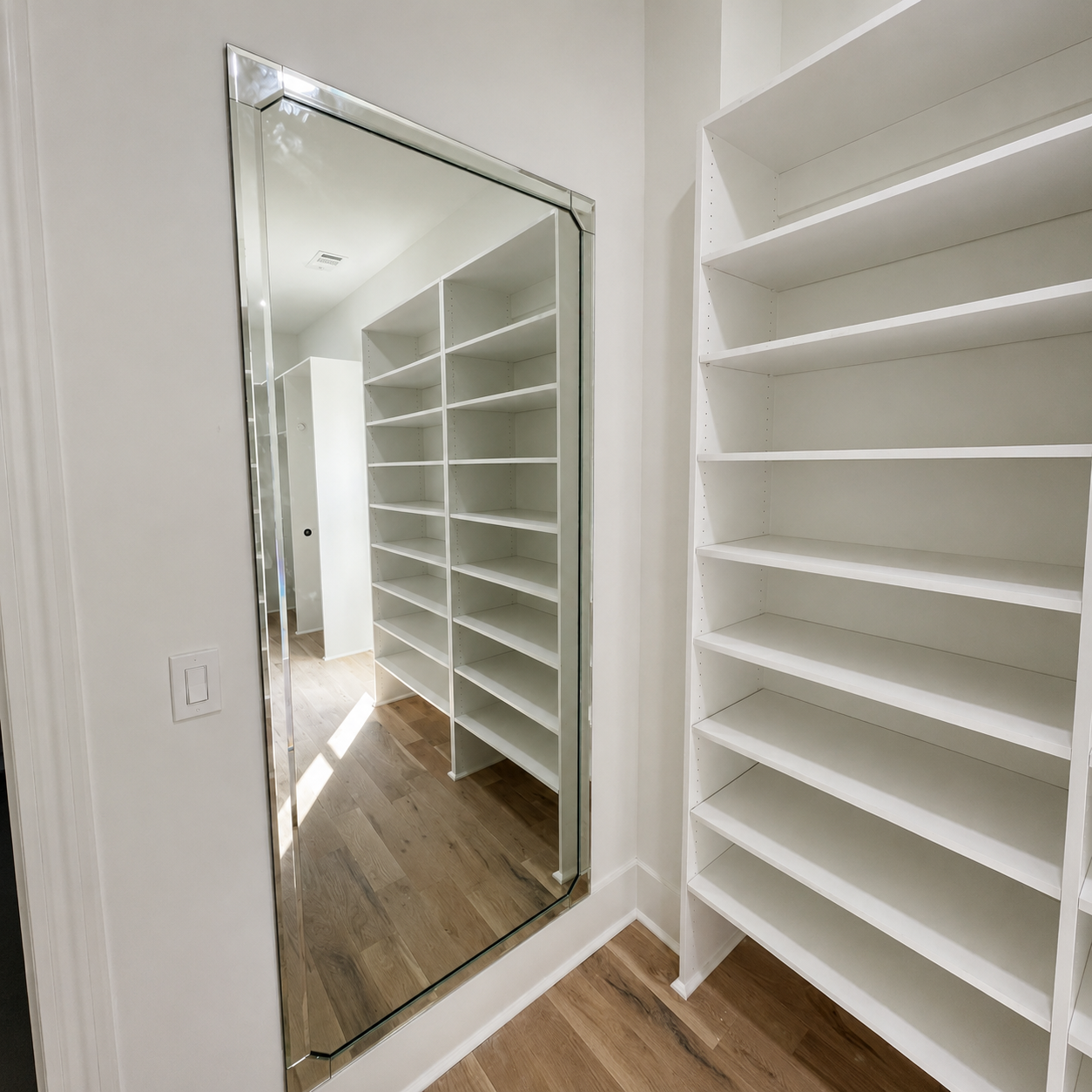 Walk-in closet with white shelves, mirrored door, and wood floor