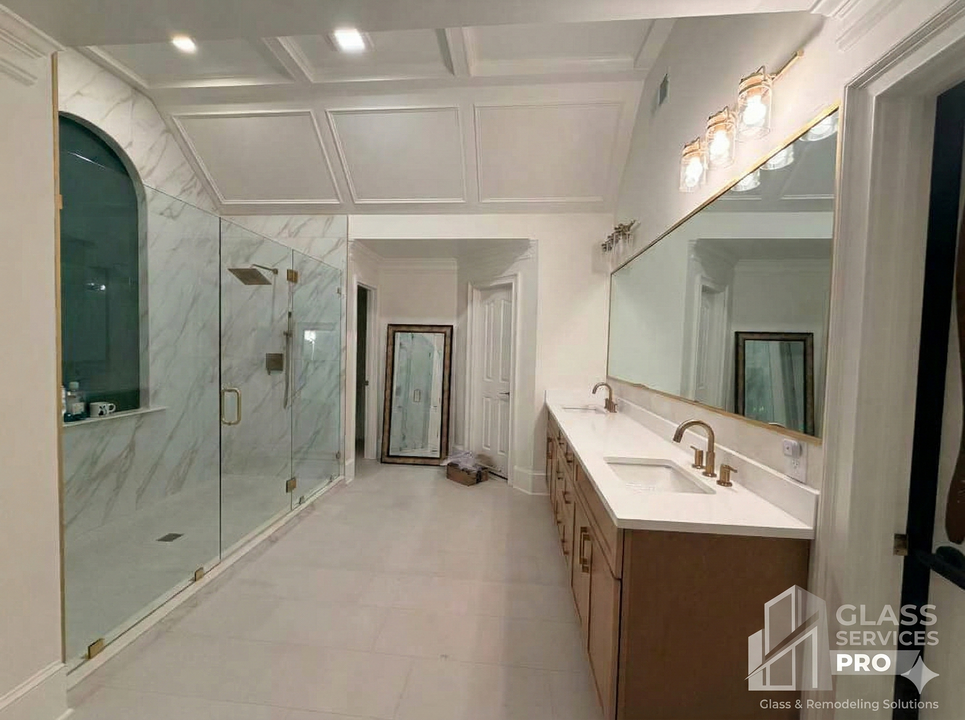 Bright modern bathroom with glass shower, long vanity, white tile, and ceiling lights.