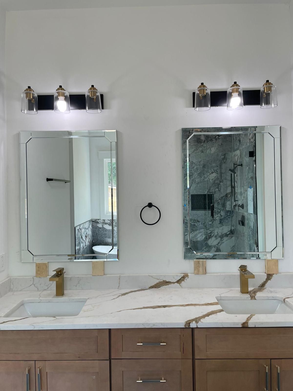 Modern bathroom vanity with two mirrors, wall sconces, white countertops, and gold faucets