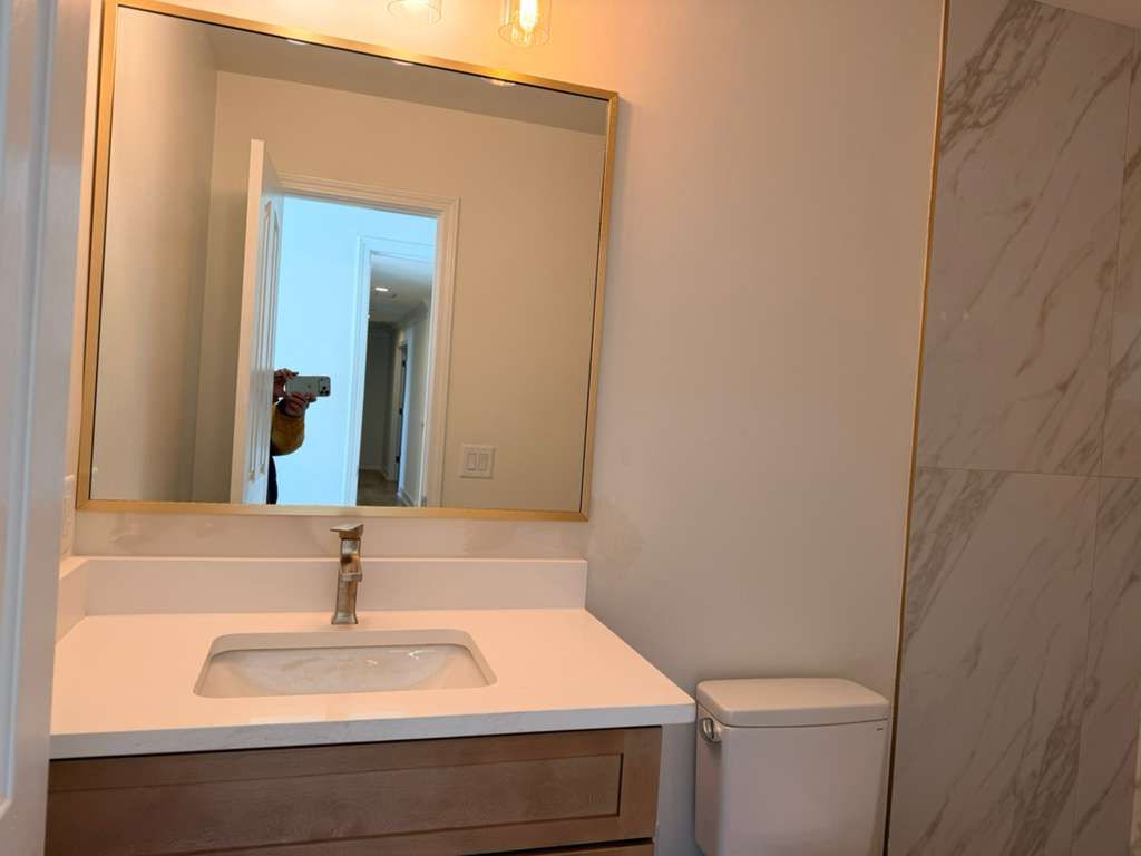 Modern bathroom with white sink, large mirror, and marble-patterned wall beside a toilet