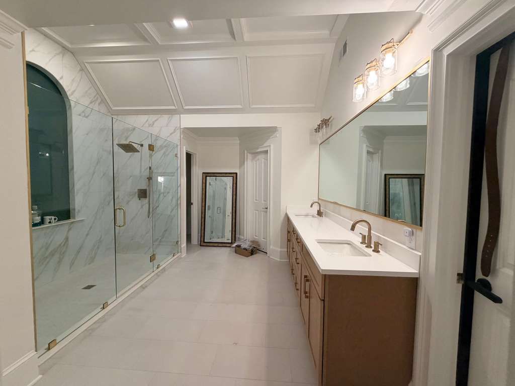 Bright bathroom with glass shower walls, white walls, and a long double vanity with lights.