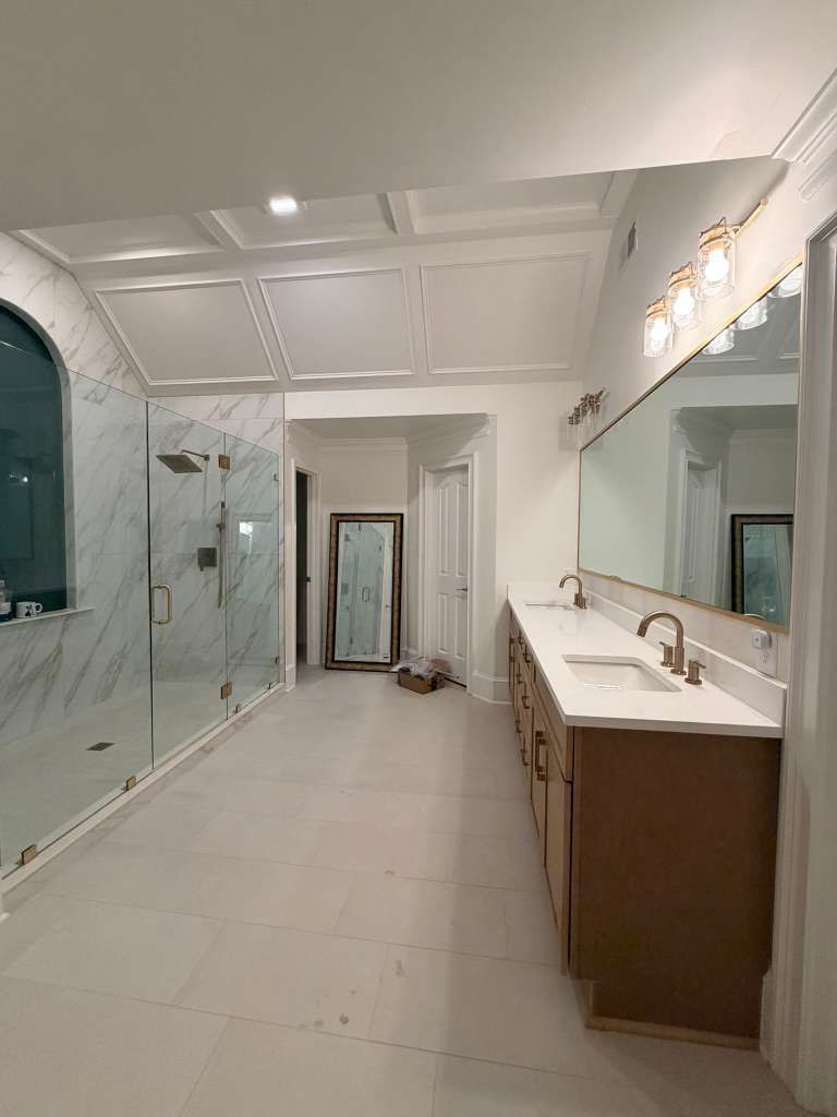 Modern bathroom with glass shower, white tile, and long vanity with mirror lights.