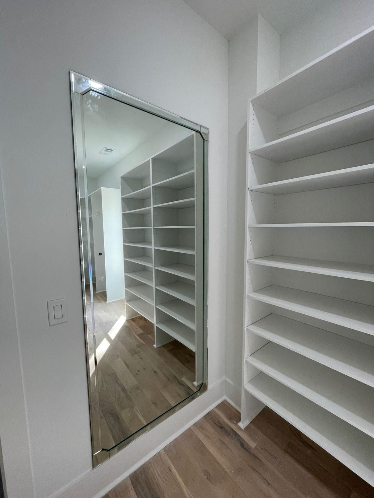 Closet room with built-in white shelves, a wall mirror, and wood flooring