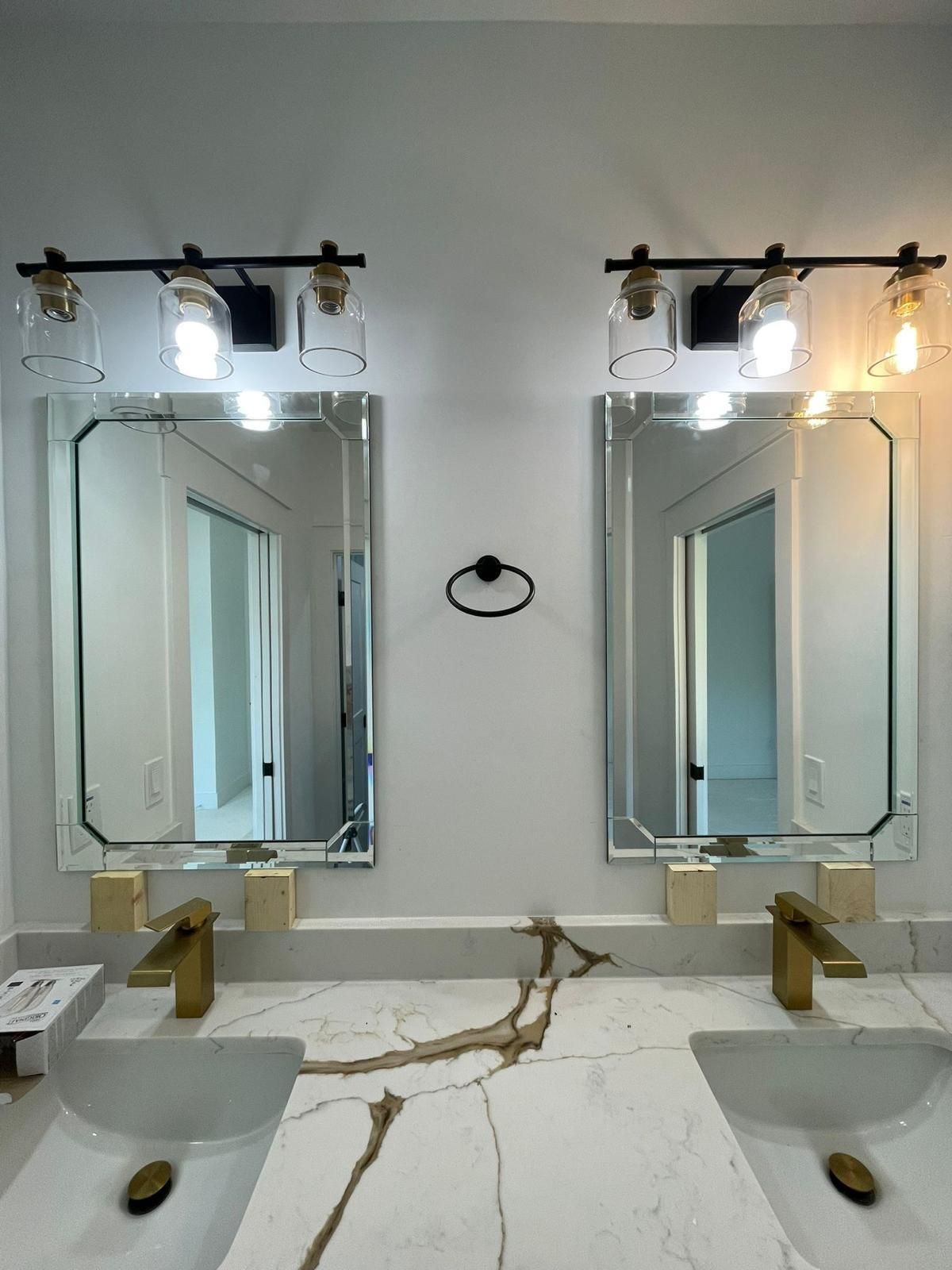 Modern bathroom with two mirrors, double sinks, and bright wall sconces over a marble countertop.