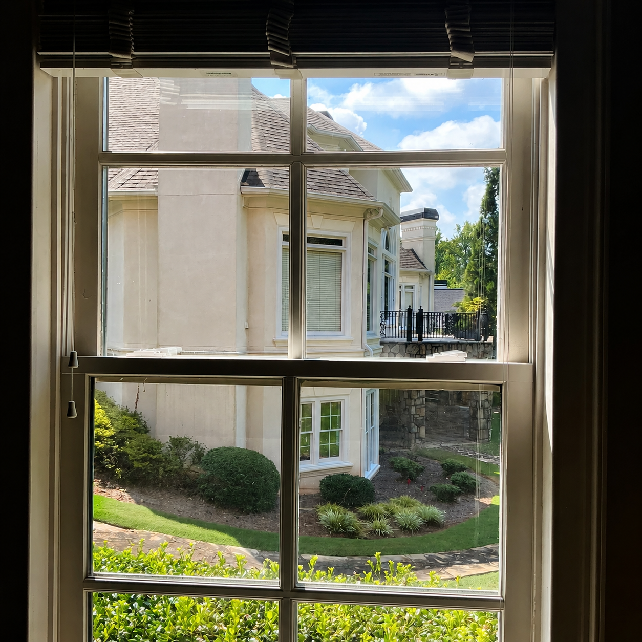 View through a window to a cream-colored house, garden, and blue sky.