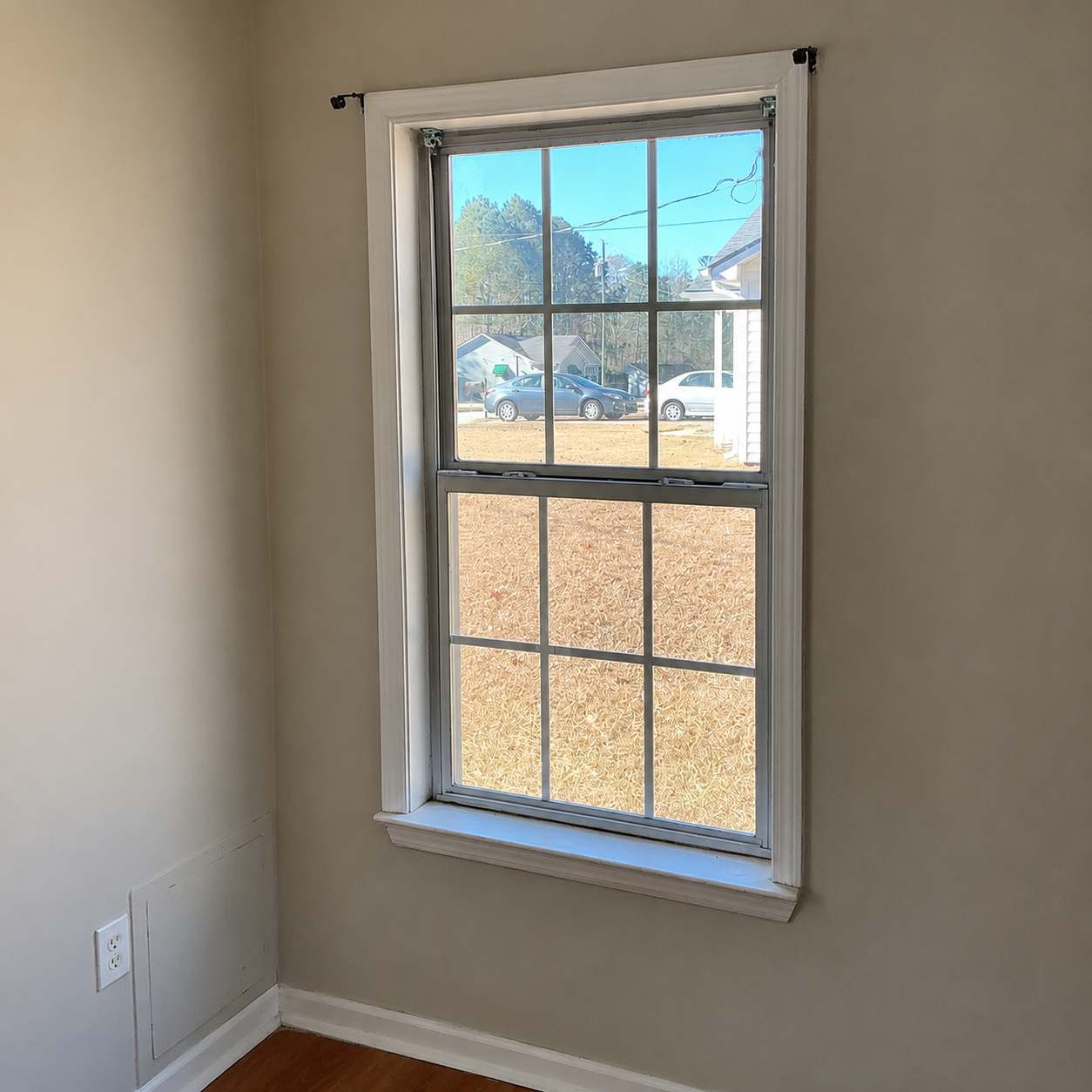 Empty beige room with a single window overlooking a yard and mountains.