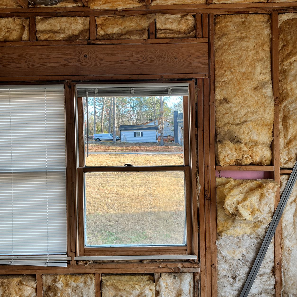 Insulated wall framing with a window looking out to a small blue shed and yard.