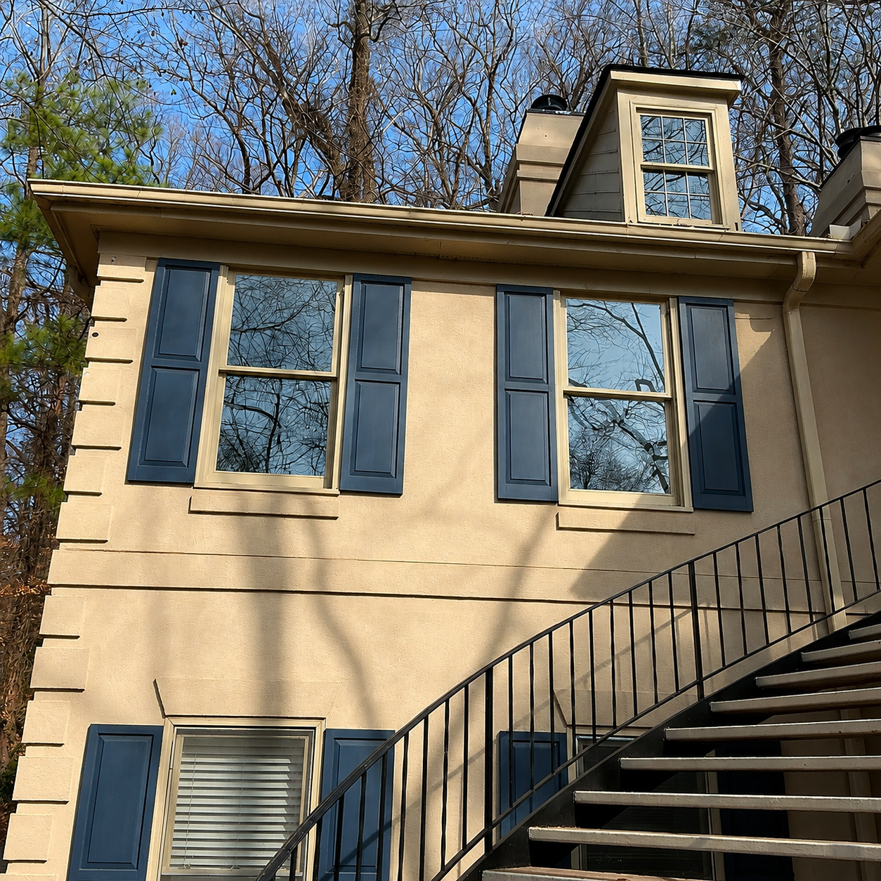 Tan house with blue shutters and an exterior staircase under a clear sky