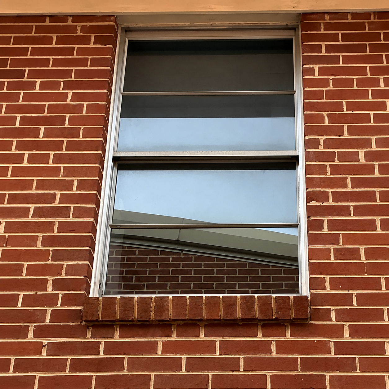 Tall narrow window set in a red brick wall, reflecting the sky and roofline.