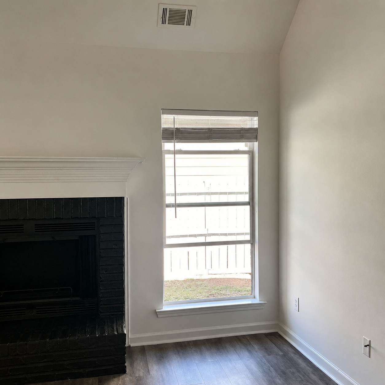Empty white room with a black fireplace, window, and hardwood floor