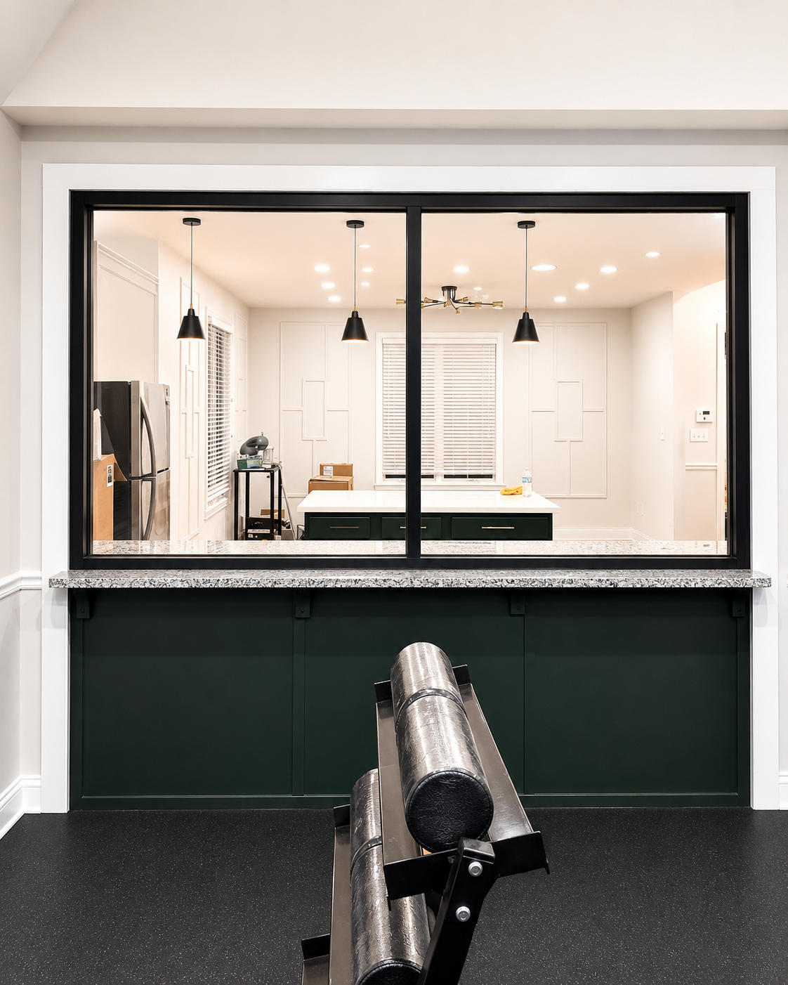 Home gym viewed through a large interior window, with a black bench and white walls behind it.