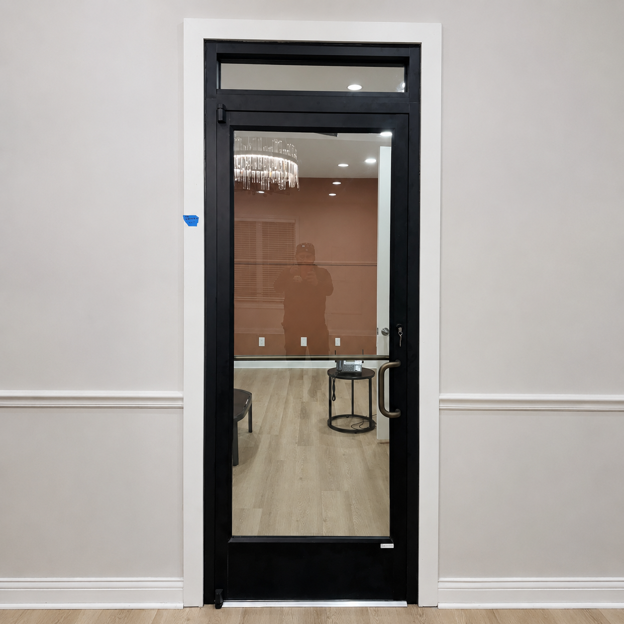 Glass office door in a white hallway, showing a conference room with a chandelier and table inside.