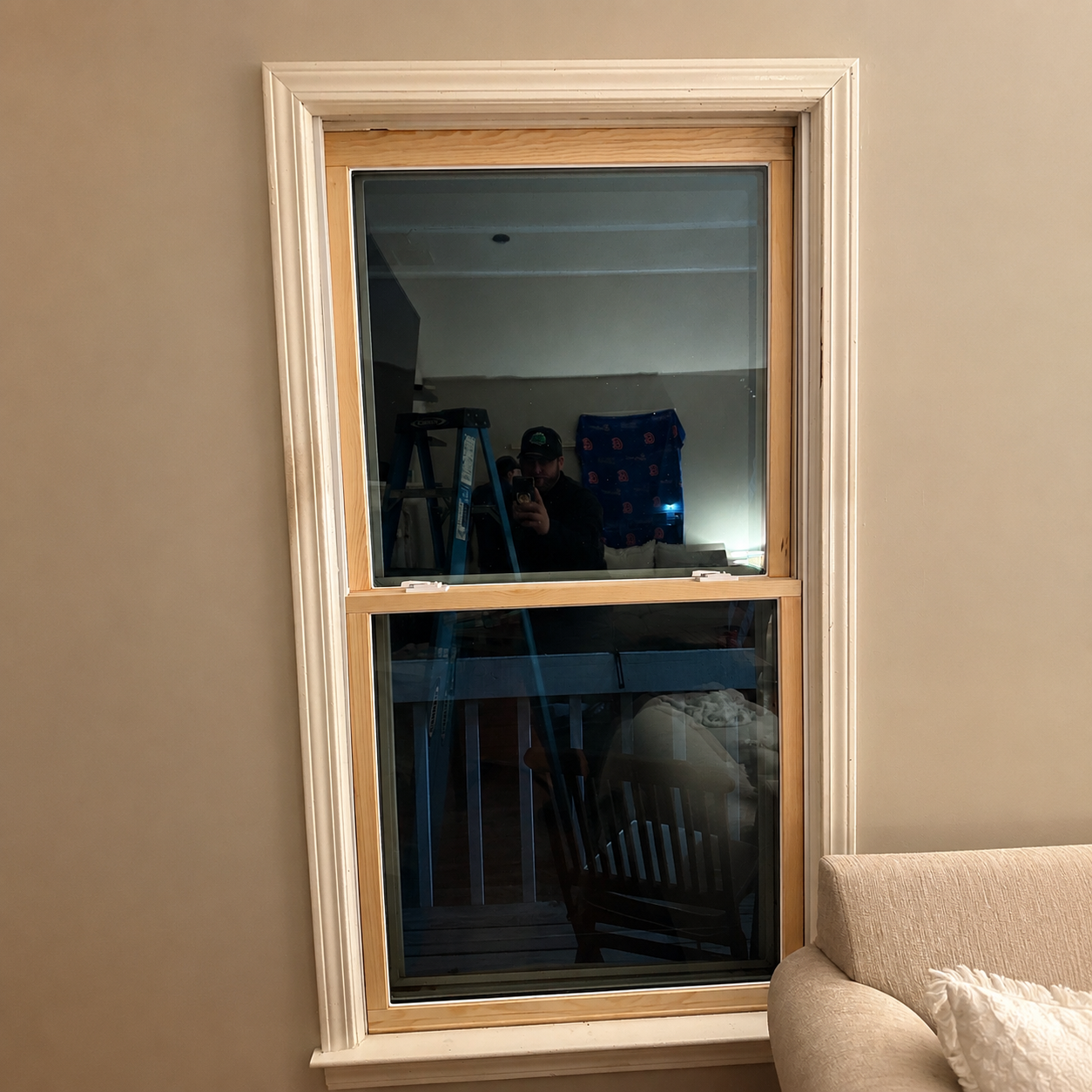 Window with beige trim reflecting a dim room, with part of a couch at the lower right.