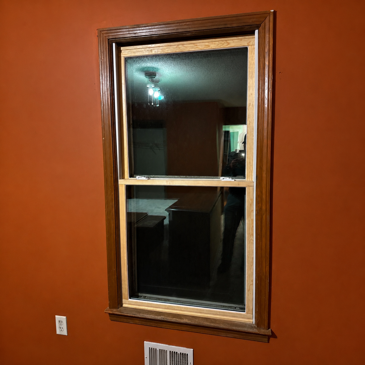 Wood-framed window on an orange wall, with a dark room reflected in the glass.