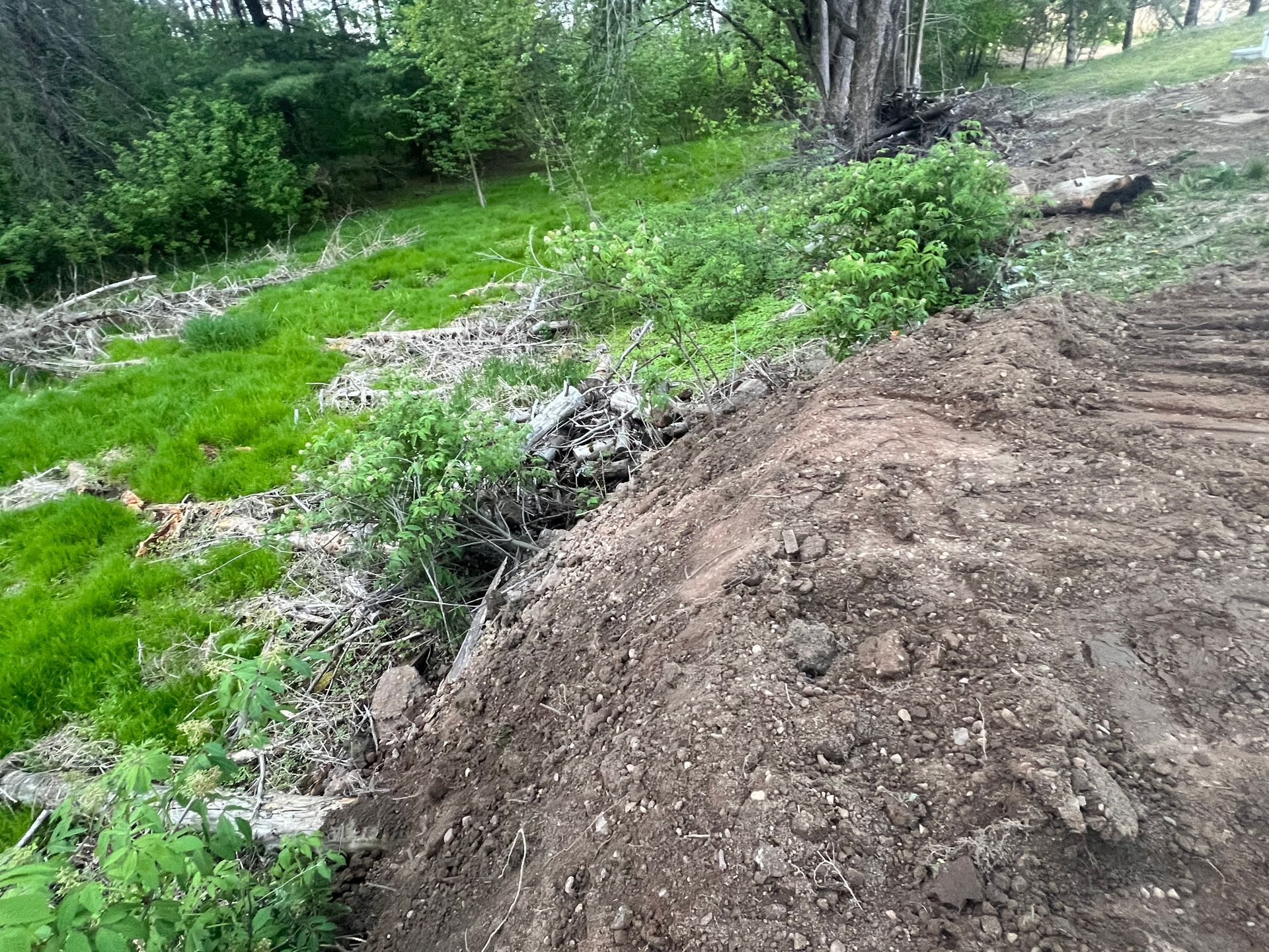 Tracked excavator grading a sloped rural Wisconsin lot with fresh soil turned and blue sky overhead during excavation work