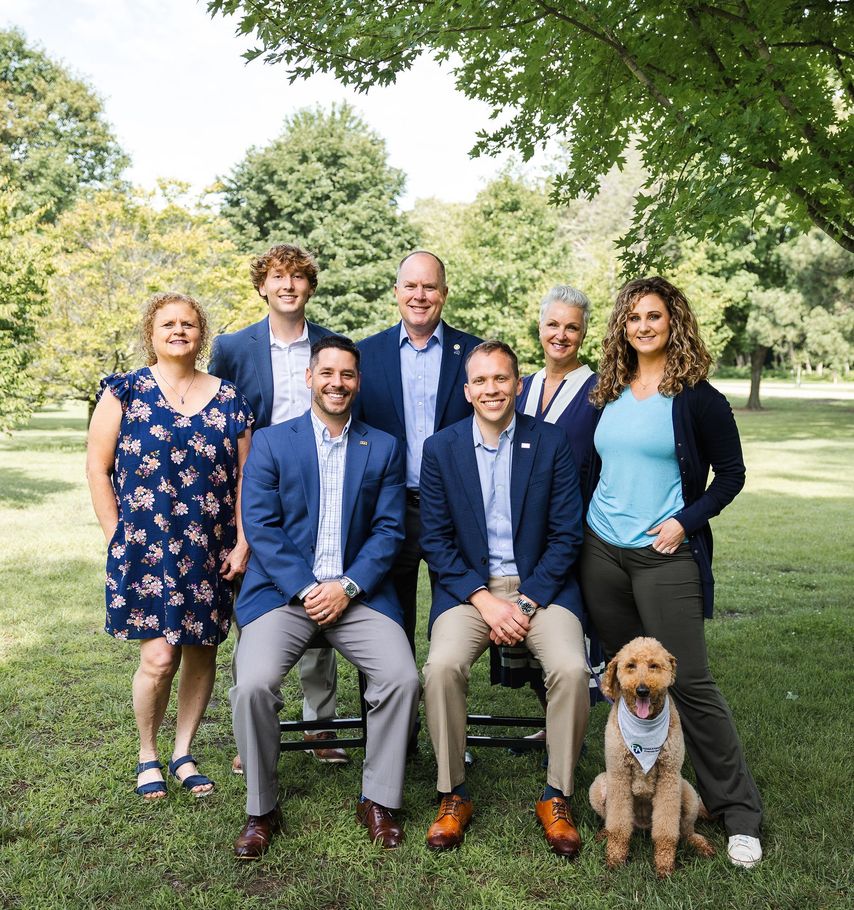 Group of seven people posing for a photo in an office setting with a dog.