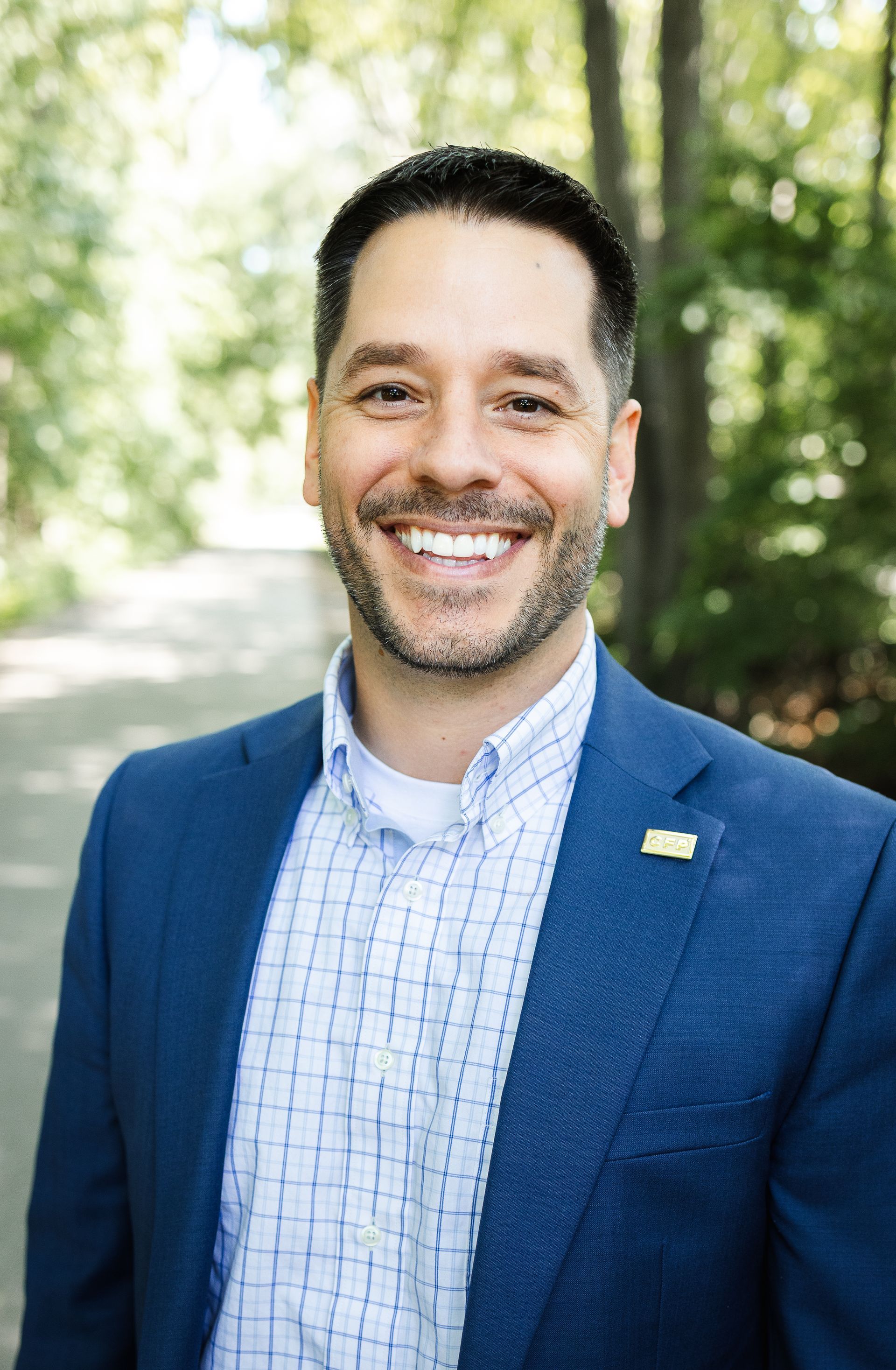 Man in blue blazer smiling, looking at the camera against a grey backdrop.