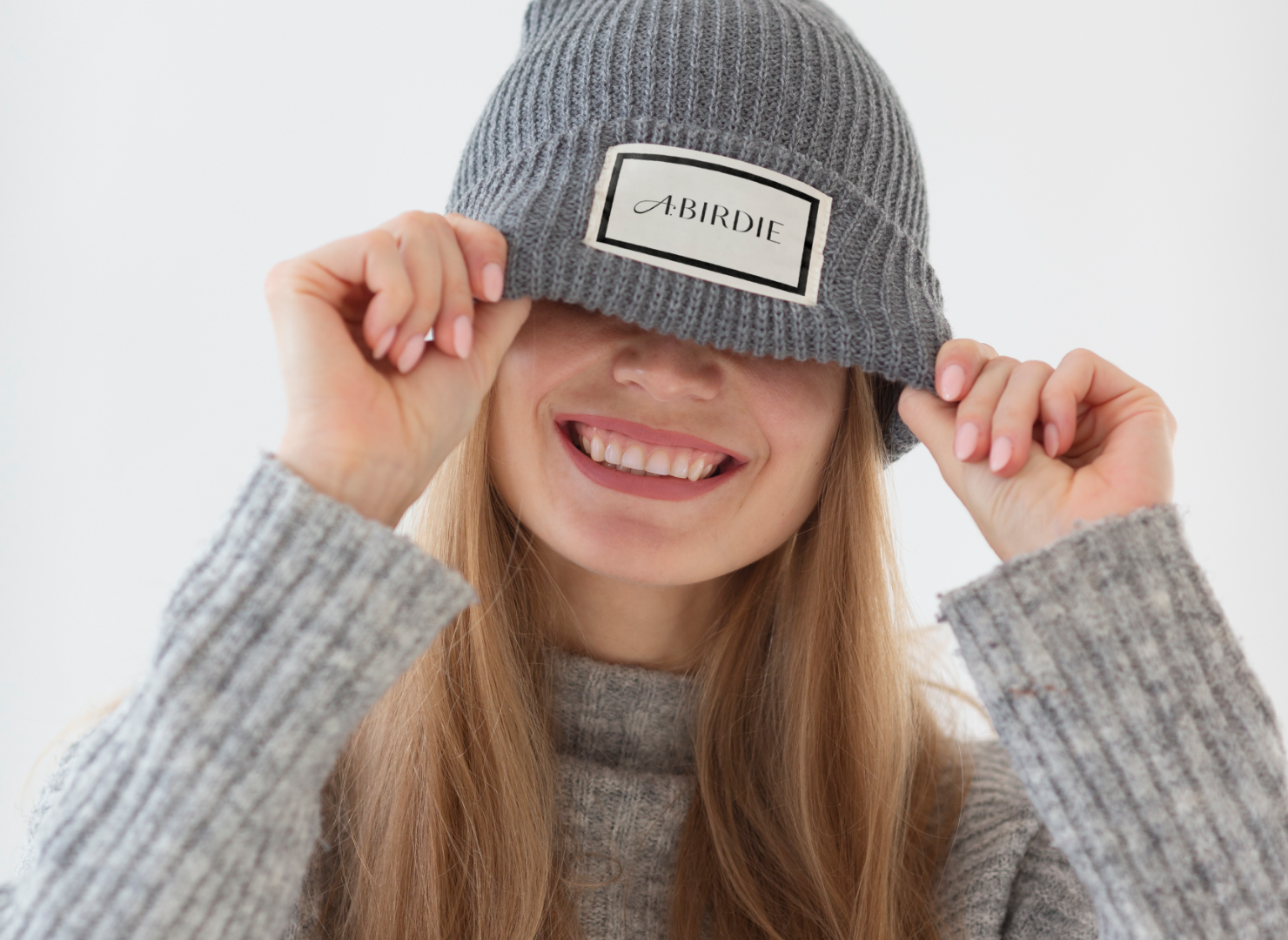 A woman wearing a sweater and a beanie is covering her eyes with her hat.