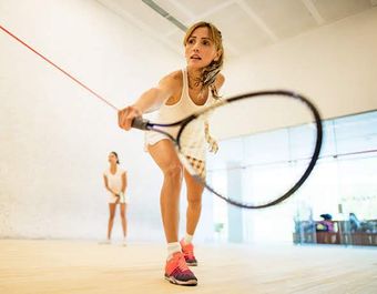 Person lunging forward in a bright studio, swinging a tennis racket toward a ball on a red string.