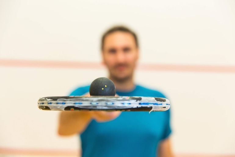 Table tennis paddle balancing a ball in front of a blurred player in a blue shirt