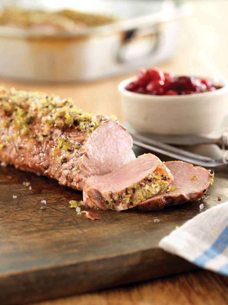 A piece of meat is sitting on a wooden cutting board next to a bowl of cranberry sauce.