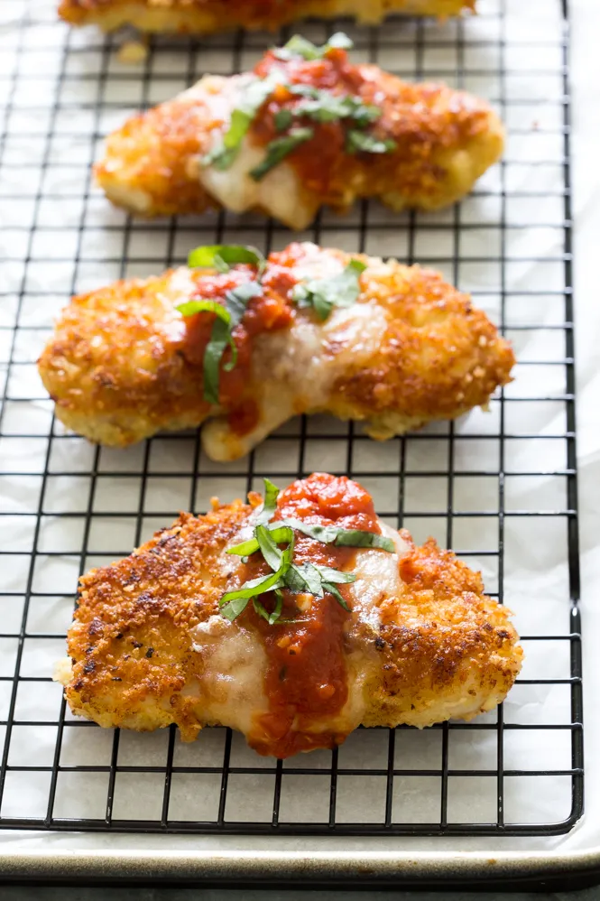Fried chicken covered in sauce and cheese is sitting on a cooling rack.