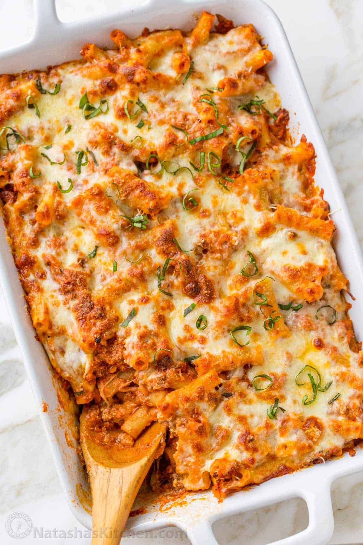 A white casserole dish filled with lasagna and a wooden spoon.