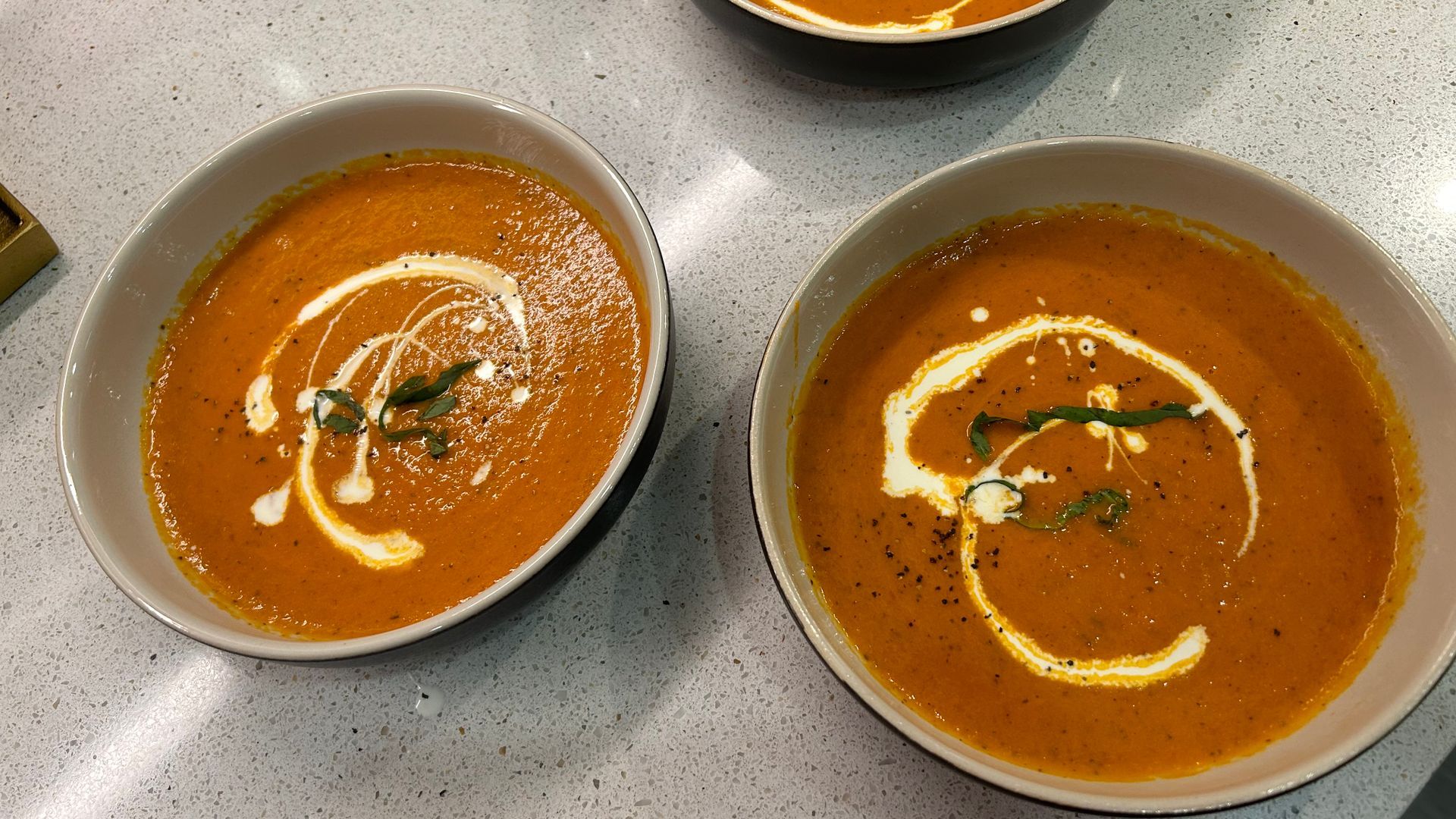 Two bowls of tomato soup with whipped cream on a table.