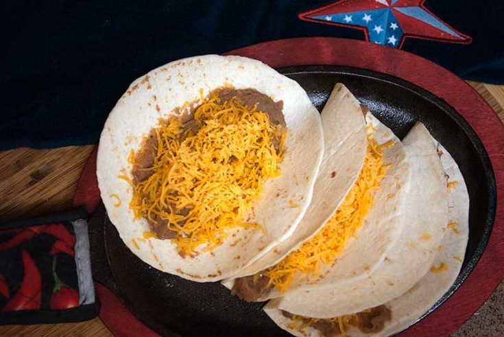 A plate of tacos with cheese and beans on a table.