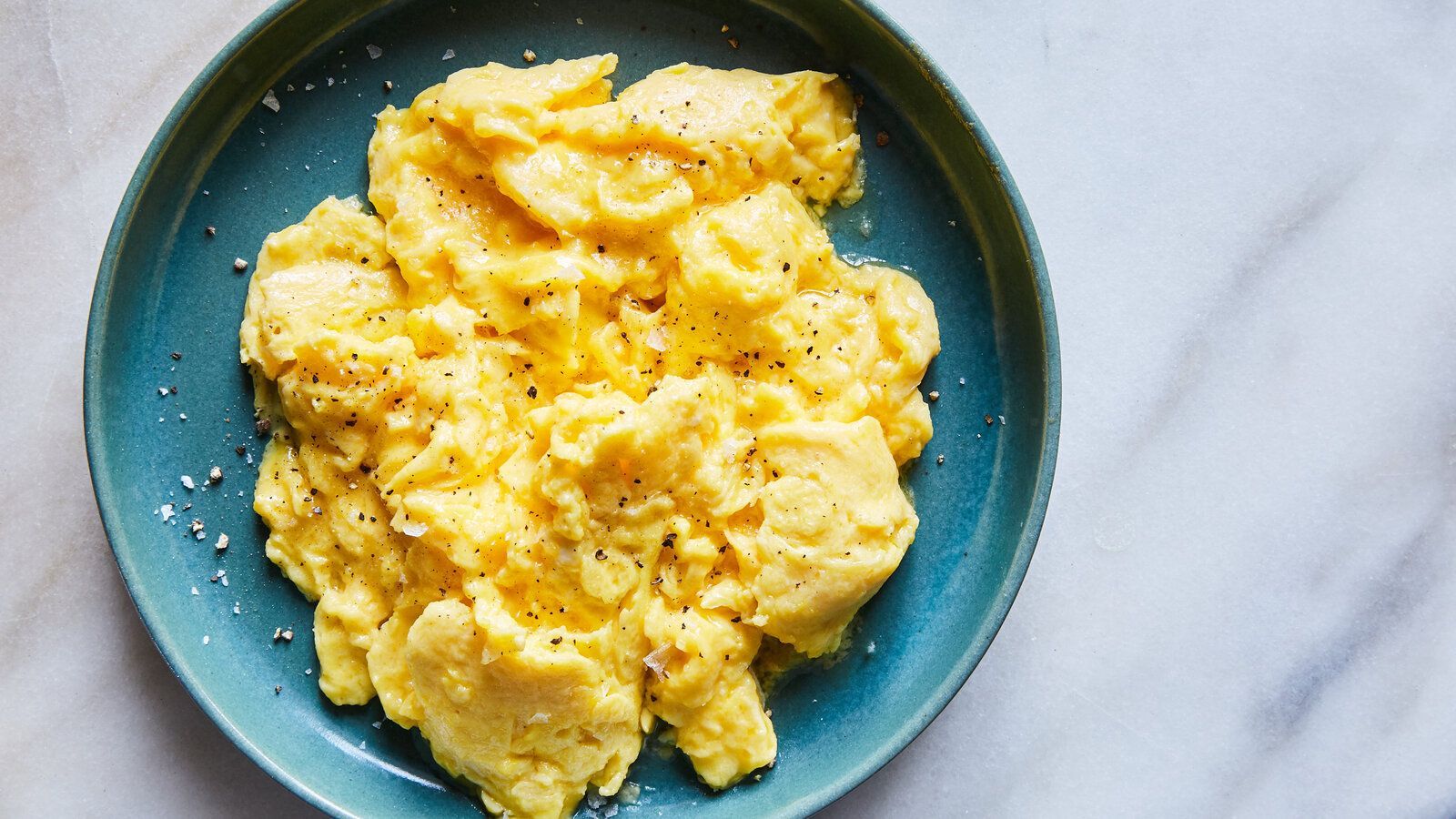 A blue plate topped with scrambled eggs on a table.