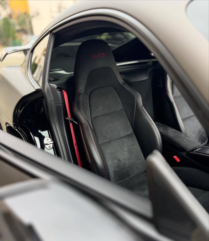 Interni sportivi di un'auto nera con sedile da corsa a vista e cinture di sicurezza rosse visibili attraverso il finestrino aperto.