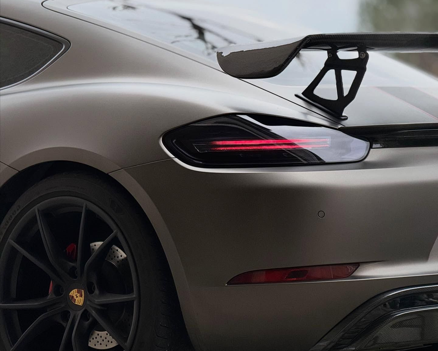 Vista posteriore di una Porsche sportiva grigio opaco con cerchi neri e un grande alettone posteriore.