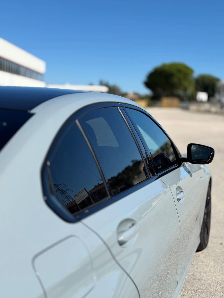 Auto bianca parcheggiata all'aperto sotto un cielo azzurro e limpido, vista laterale con vetri oscurati.
