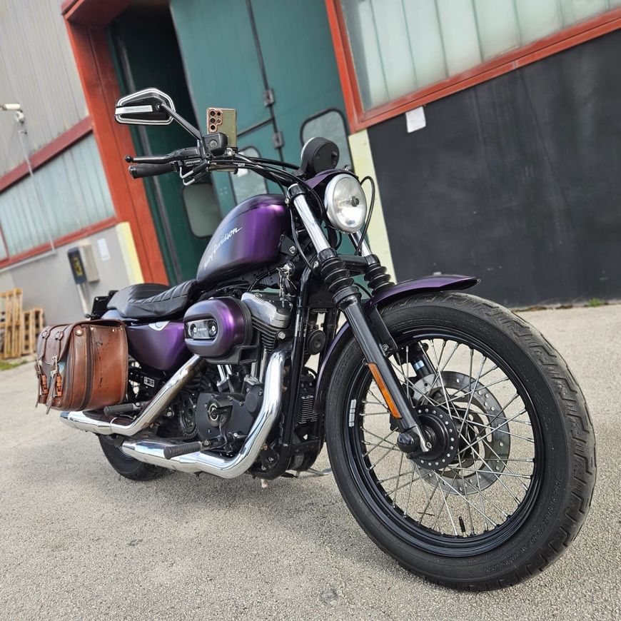 Una motocicletta cruiser viola è parcheggiata davanti a un edificio industriale con pareti nere e finiture rosse.
