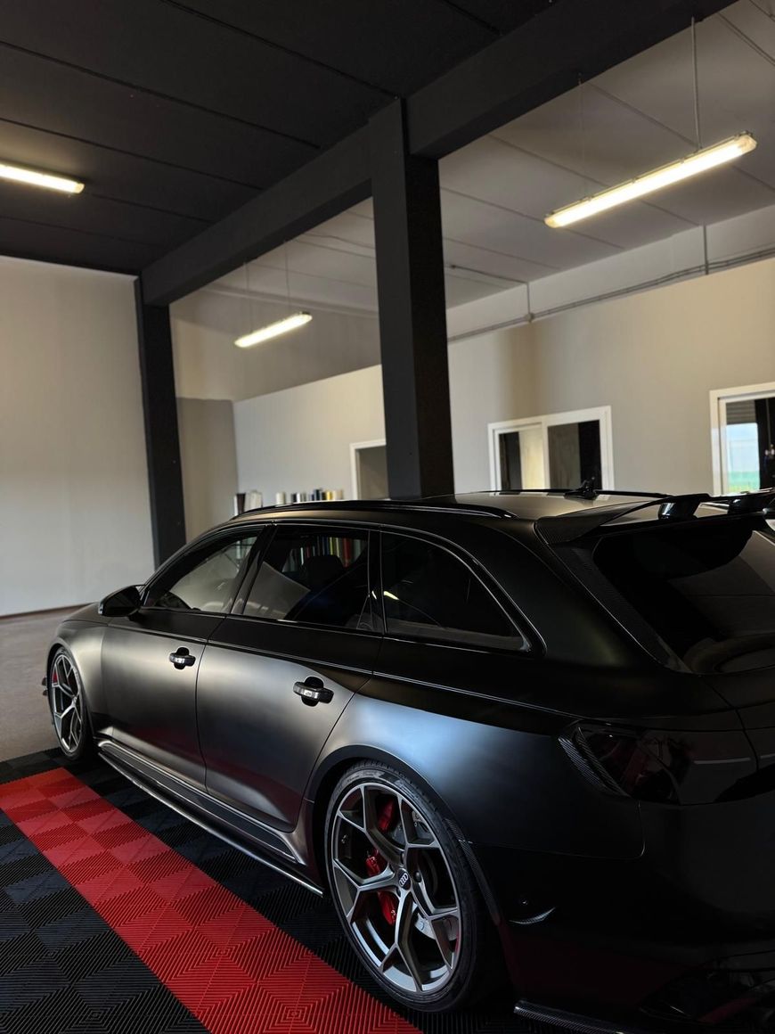 Station wagon sportiva nera opaca in uno showroom con pareti bianche e dettagli in moquette rossa
