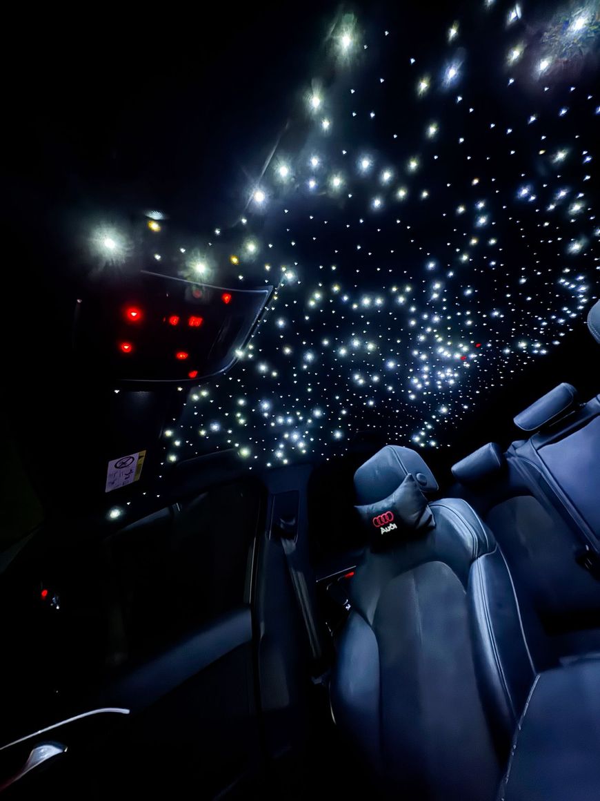 Interni di un'auto con luci a soffitto effetto cielo stellato e sedili scuri, come l'abitacolo di un veicolo di lusso o a tema.